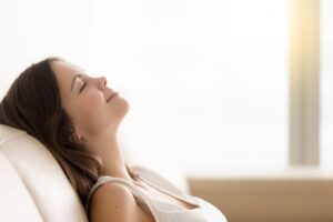 Relaxed woman who is reclining on a beige couch in the sunlight